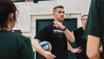 Jake Barreau holding a ball and speaking with athletes at practice