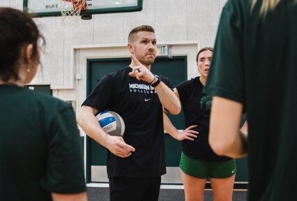 Jake Barreau holding a ball and speaking with athletes at practice