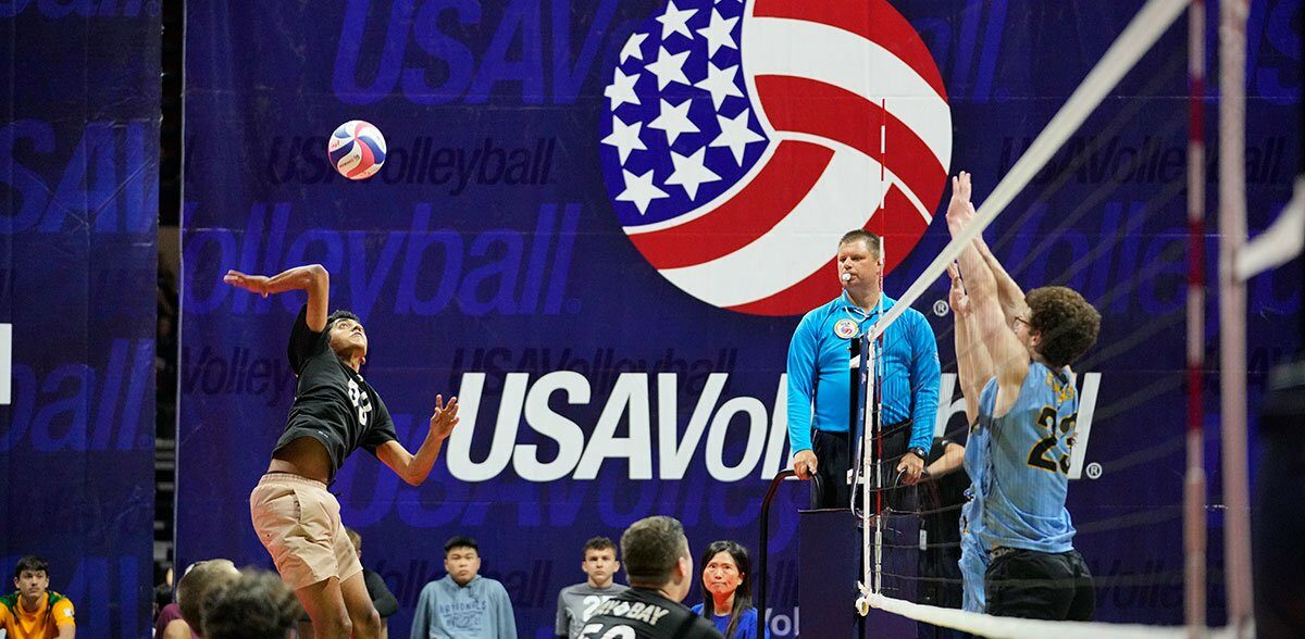 boys volleyball player attacking against a double block
