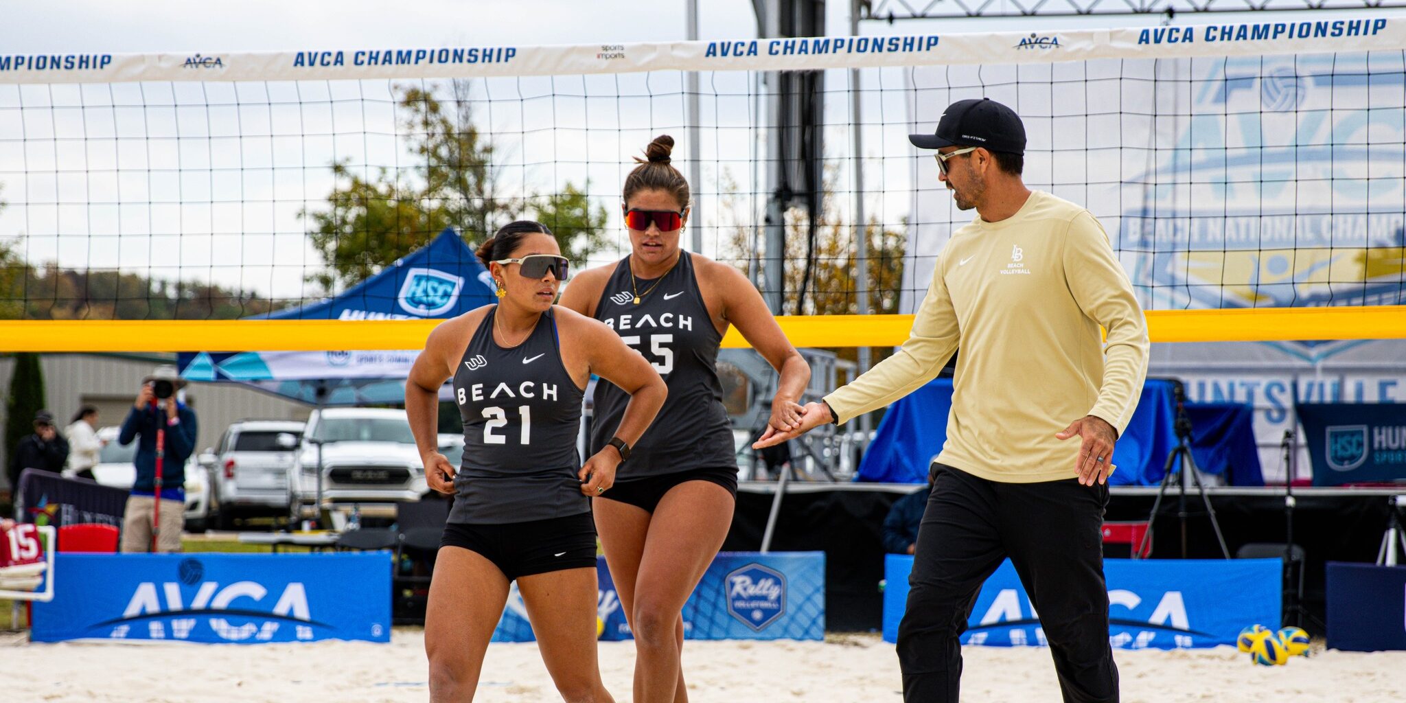 Mike Campbell walking and talking to two Long Beach State beach volleyball players